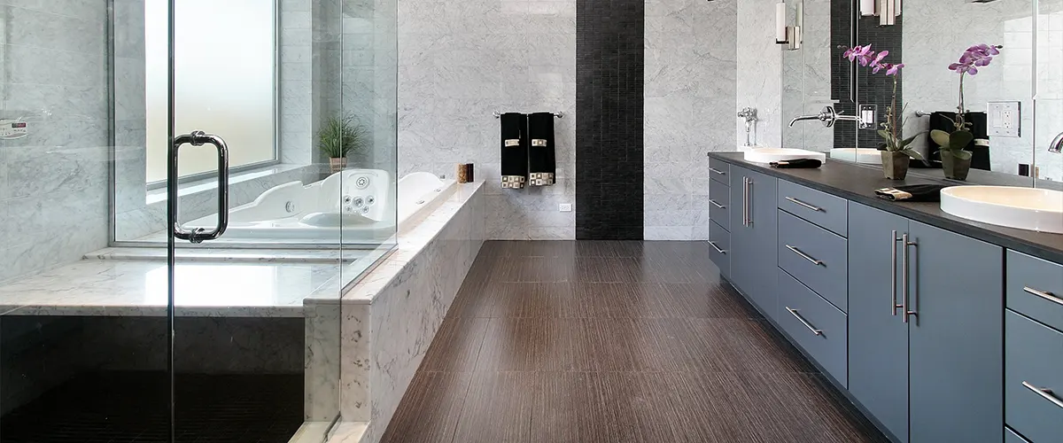 A modern bathroom with a blue double vanity, a whirlpool tub, and a glass shower