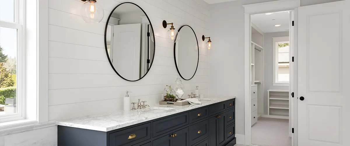 A dark blue double vanity with two round mirrors and lights