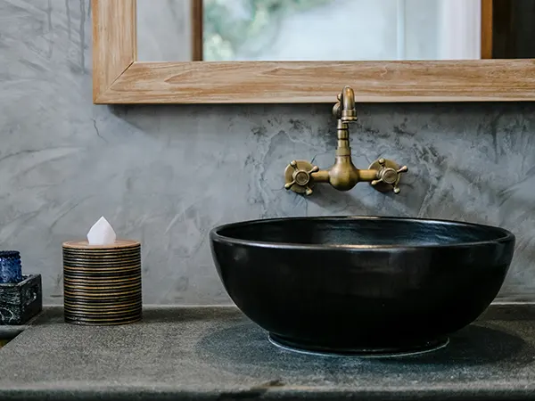 Black sink with golden fixtures and wood frame mirror