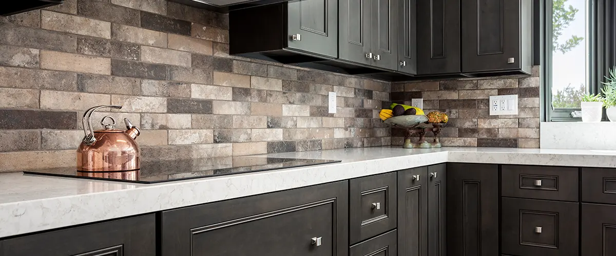 A kitchen with dark cabinets and a dark tile backsplash