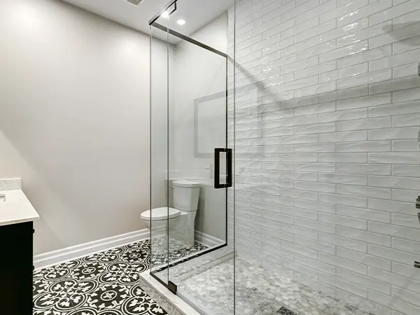 A glass-shower with a dark handle and a floor with a beautiful design