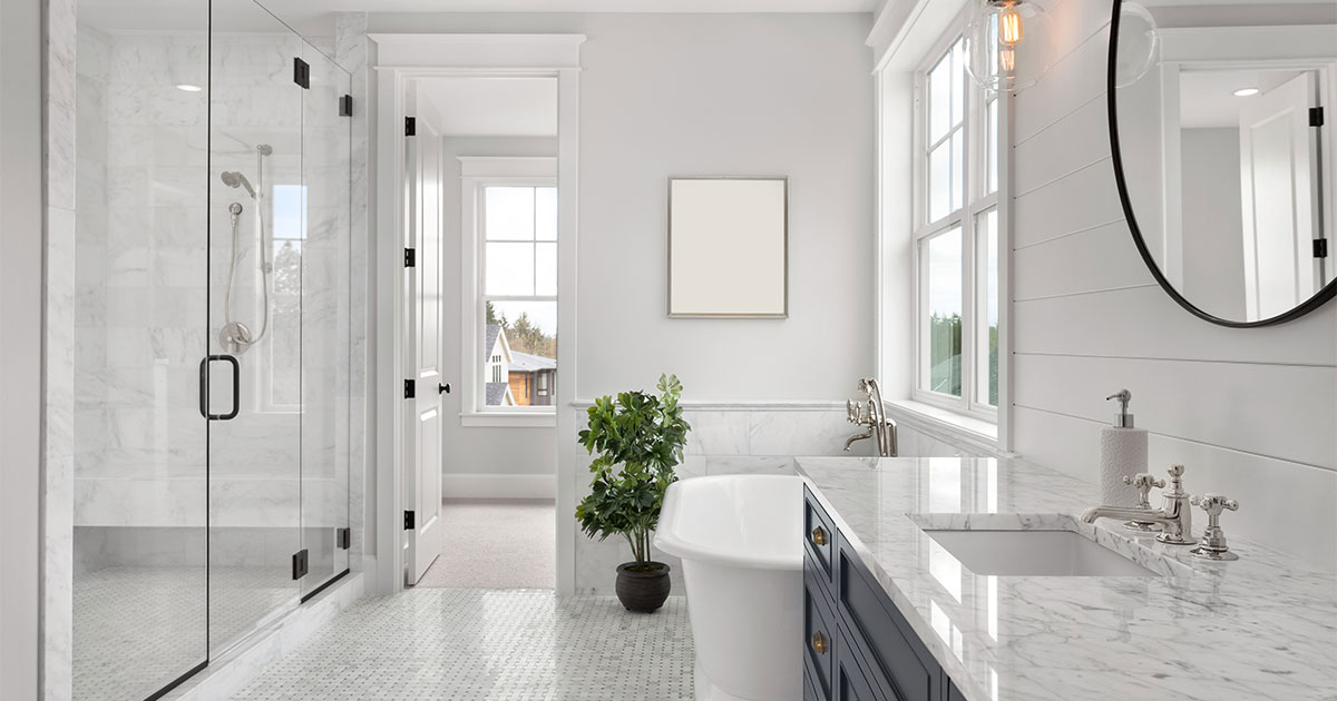 A white bathroom with double vanity, round mirror, a glass shower, and a plant