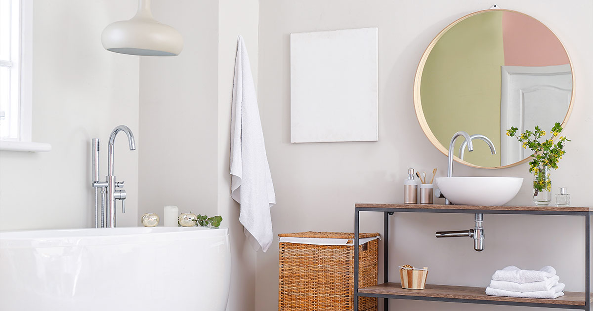 A white bathroom with minimalistic vanity, bathtub, and a round mirror