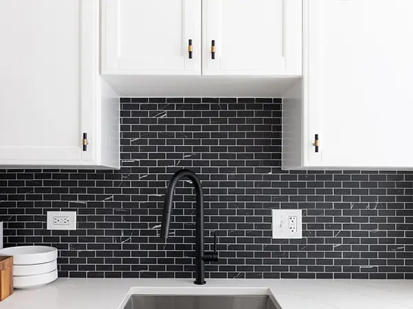 A black backsplash with a black faucet and white cabinets