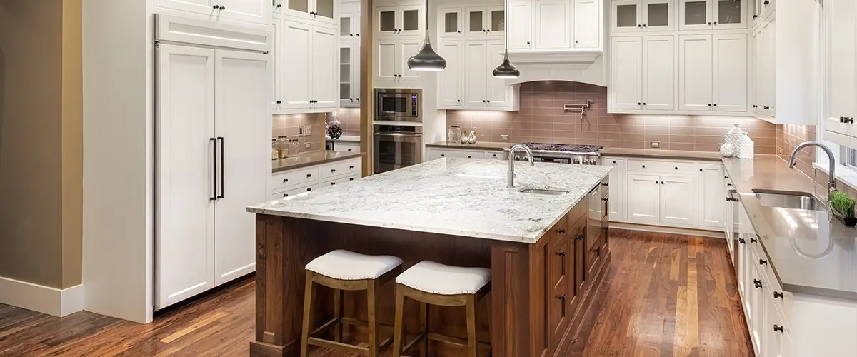 A wood kitchen island with quartz counters and white cabinets with black knobs and pulls