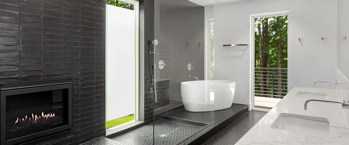 A frameless glass shower with a freestanding tub on black tile surround
