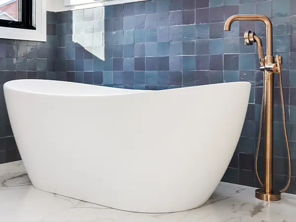 A freestanding tub with a golden faucet and blue tile walls