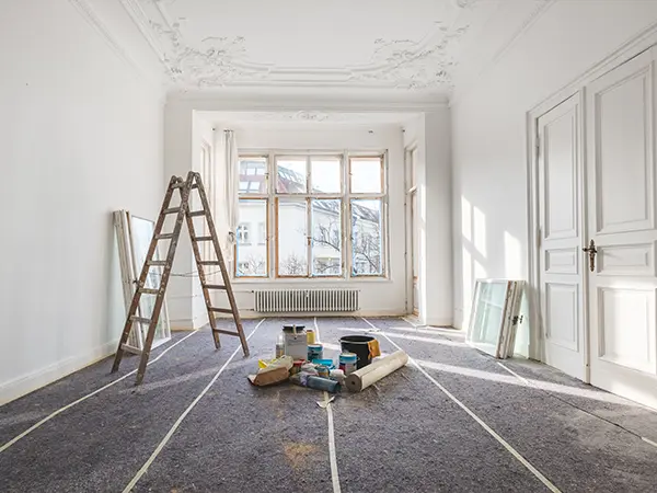 A renovation process in a room with large windows and a ladder
