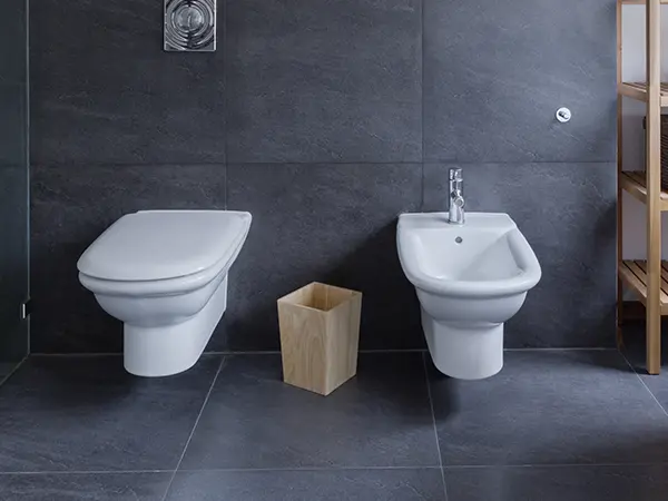 A toilet in a bathroom with dark tile flooring and walls