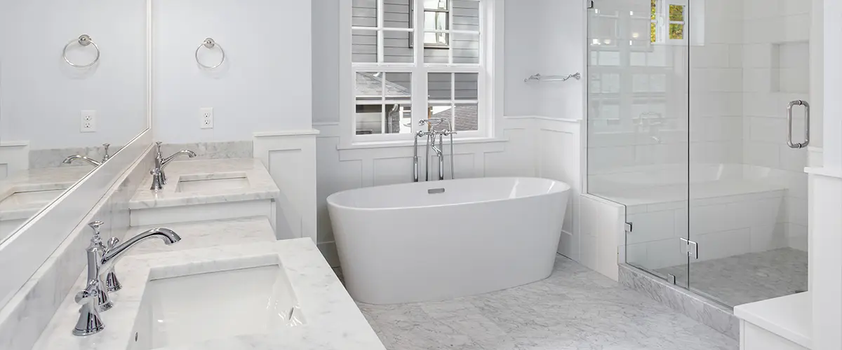 A white bathroom with a double vanity, a glass walk-in shower and a freestanding tub